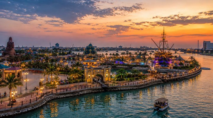 جزيرة السندباد على ضفاف نهر شط العرب وقت غروب الشمس مع إضاءة ليلية وقارب في المياه.