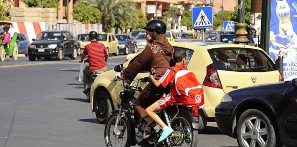 امرأة تقود دراجة نارية برفقة طفلين في أحد شوارع المدينة وسط حركة المرور والسيارات