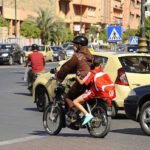 امرأة تقود دراجة نارية برفقة طفلين في أحد شوارع المدينة وسط حركة المرور والسيارات 