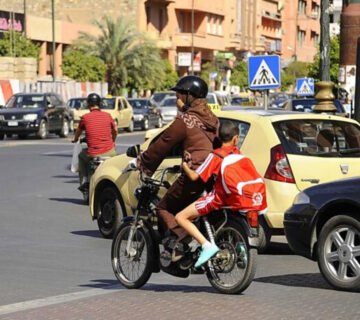 امرأة تقود دراجة نارية برفقة طفلين في أحد شوارع المدينة وسط حركة المرور والسيارات 