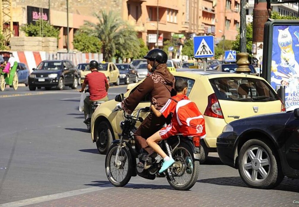 امرأة تقود دراجة نارية برفقة طفلين في أحد شوارع المدينة وسط حركة المرور والسيارات