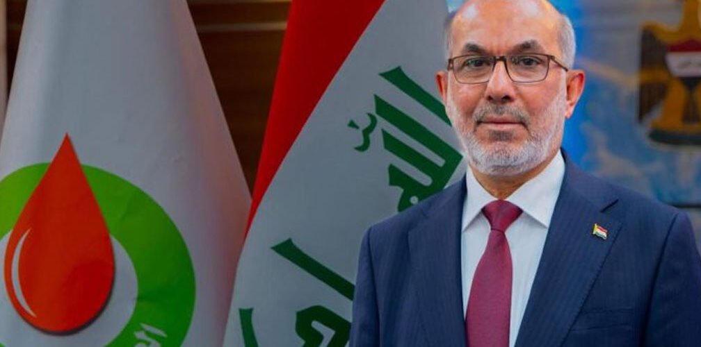 وزير النفط العراقي باسم خضير العبادي يقف أمام العلم العراقي وشعار وزارة النفط العراقية 