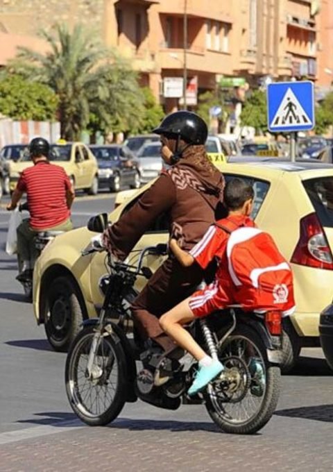 امرأة تقود دراجة نارية برفقة طفلين في أحد شوارع المدينة وسط حركة المرور والسيارات.
