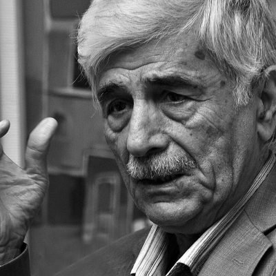 صورة بالأبيض والأسود للشاعر العراقي كاظم الحجاج أثناء حديثه في لقاء ثقافي.
